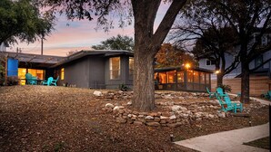 Una casa con pared de piedra, un árbol y mobiliario exterior.