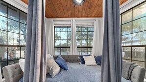Una habitación con un ventanal grande, un sofá gris con cojines azules y blancos, y un techo de madera.