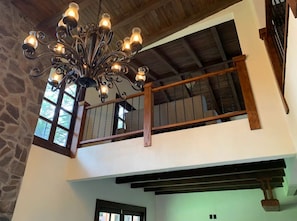 Ein mehrgeschossiges Interieur mit einem schmiedeeisernen Chandelier, Steinwänden und einem Holzbalkon.