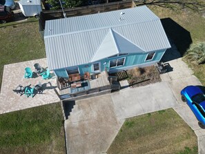 A two-story house with a patio, outdoor seating, and a blue car parked nearby.