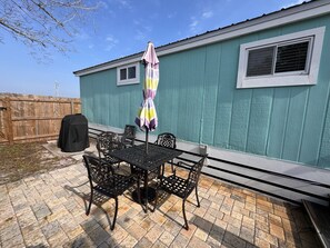 A patio with a table and chairs, a covered umbrella, and a barbecue grill.