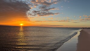 A beach with a sunset, calm water, and a distant shoreline.