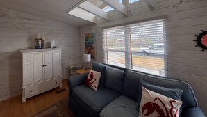A room with a wooden ceiling, a white cabinet, a blue sofa with red pillows, a lamp, and a painting. - STEPS TO THE BEACH
WELCOME TO PARADISE (Mexico Beach)