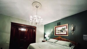 A bedroom with a bed, a wooden wardrobe, a chandelier, a framed picture on the wall, and a nightstand with a lamp. - One-of-a-kind historic getaway, where timeless charm meets modern fun & comfort. (Front Royal)