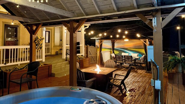 A covered outdoor patio with a hot tub, wooden deck, and string lights. - One-of-a-kind historic getaway, where timeless charm meets modern fun & comfort. (Front Royal)