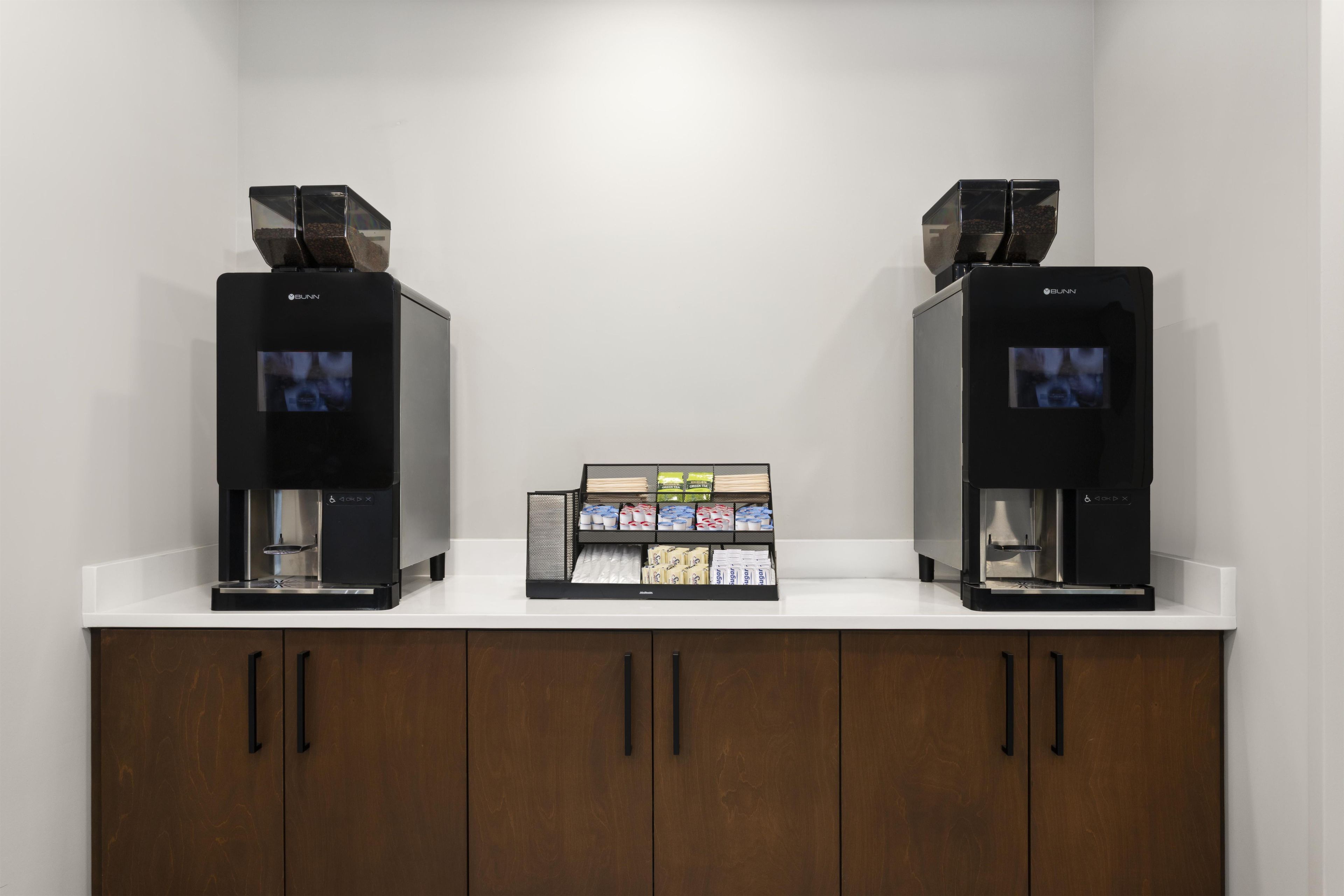 Dos máquinas de café sobre una encimera blanca, con un expositor de granos de café en el centro.
