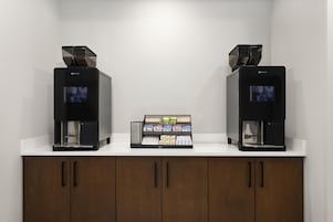 Dos máquinas de café sobre una encimera blanca, con un expositor de granos de café en el centro.