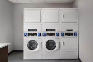 A laundry area with four stacked washing machines and a single dryer. - @HOME by Best Western McDonough Atlanta South (McDonough)