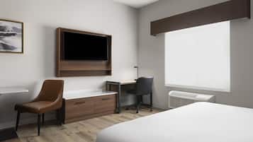 A hotel room with a bed, a desk with a chair, a television mounted on the wall, and a window.
