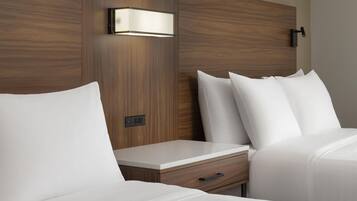 A hotel room with a wooden headboard, a bedside table with a drawer, and a wall-mounted light fixture.