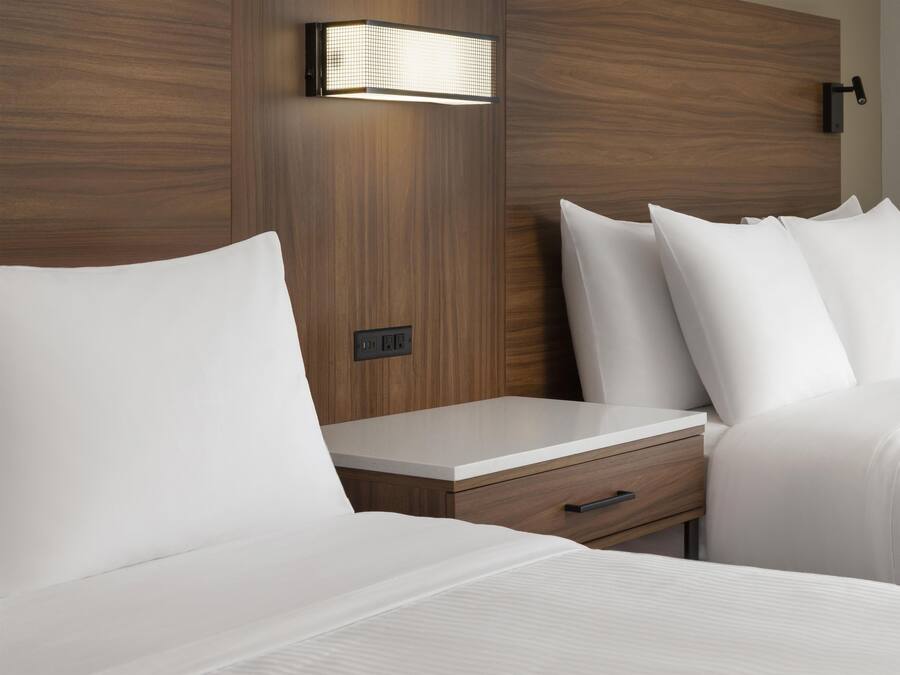 A hotel room with a wooden headboard, a bedside table with a drawer, and a wall-mounted light fixture.