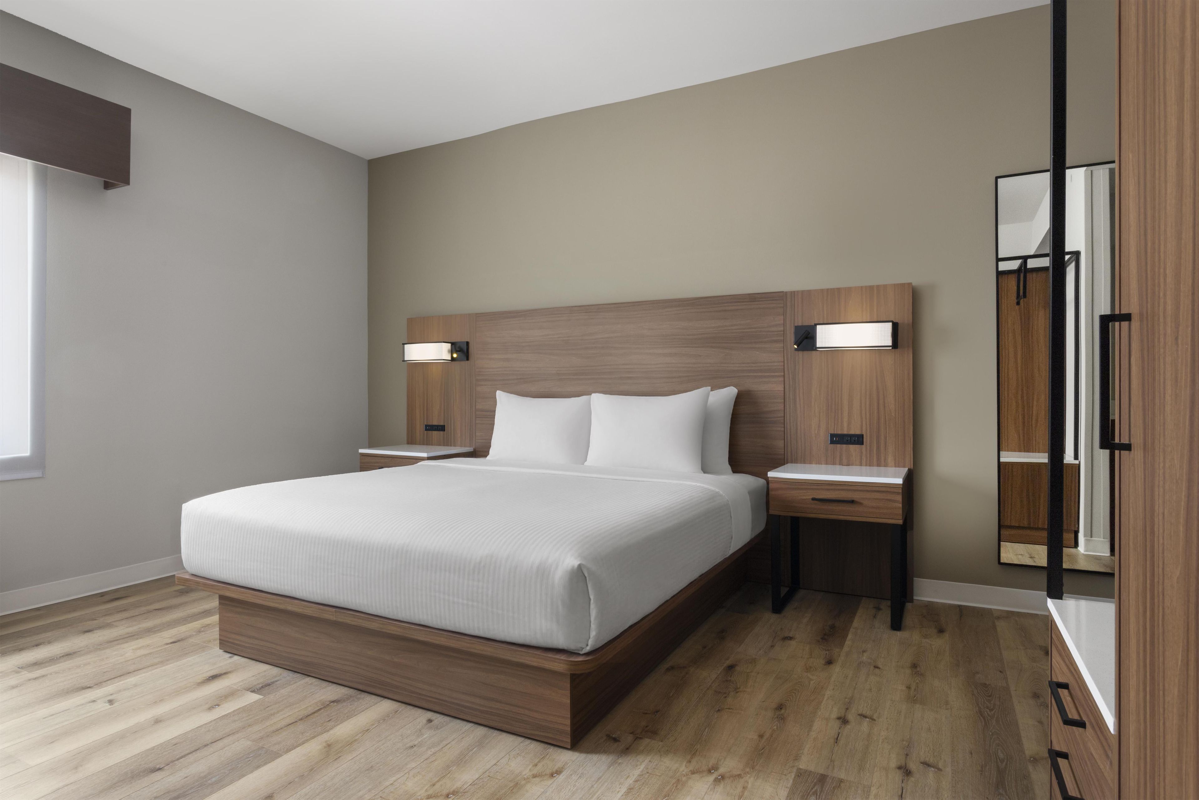 Ein modernes Schlafzimmer mit einem großen Bett, einem Holzkopfende, Nachttischen und einem Spiegel.