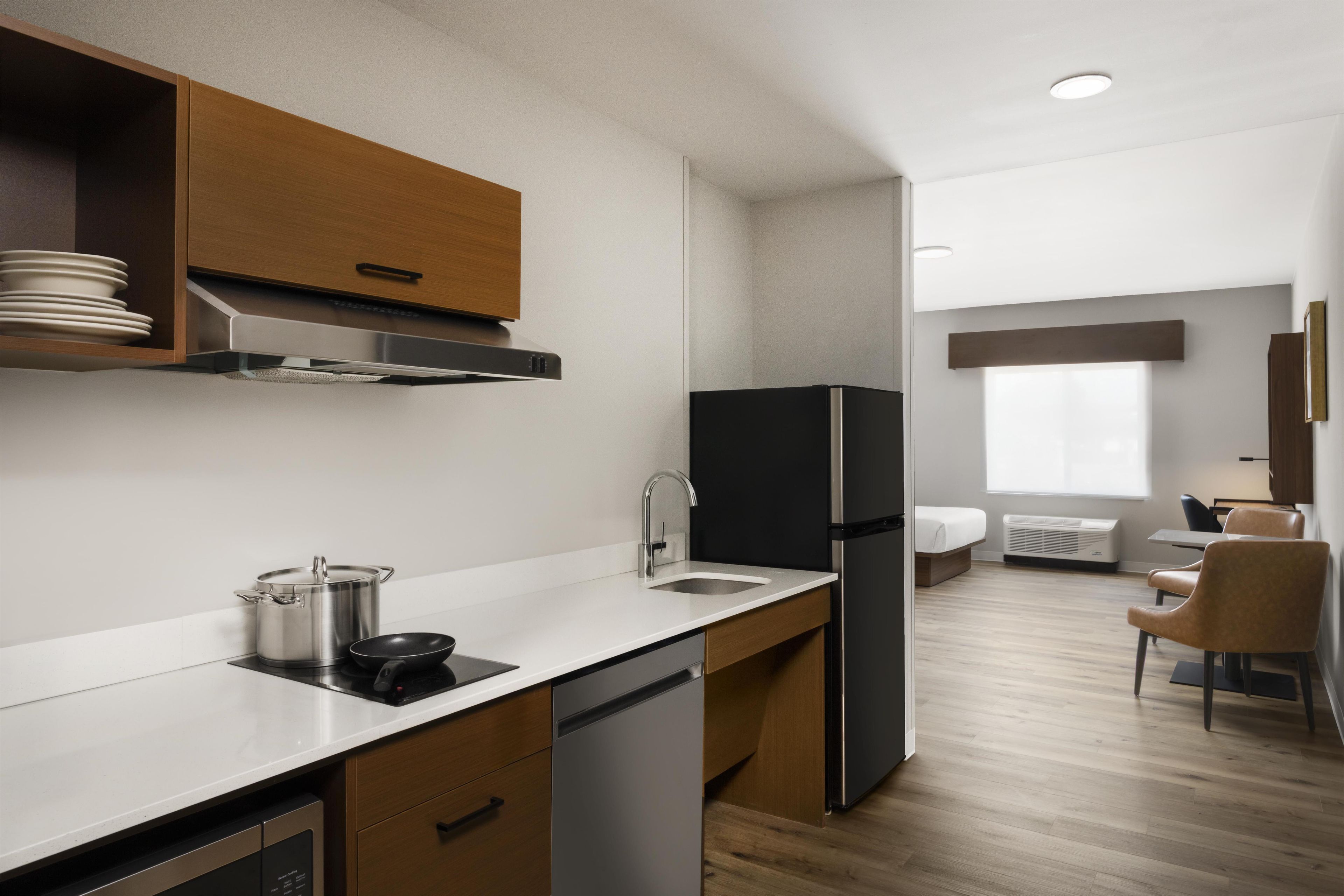 Una cocina moderna con estufa integrada, pileta y refrigerador negro. Hay un mueble de madera sobre la estufa y un pequeño comedor con una silla y una mesa.