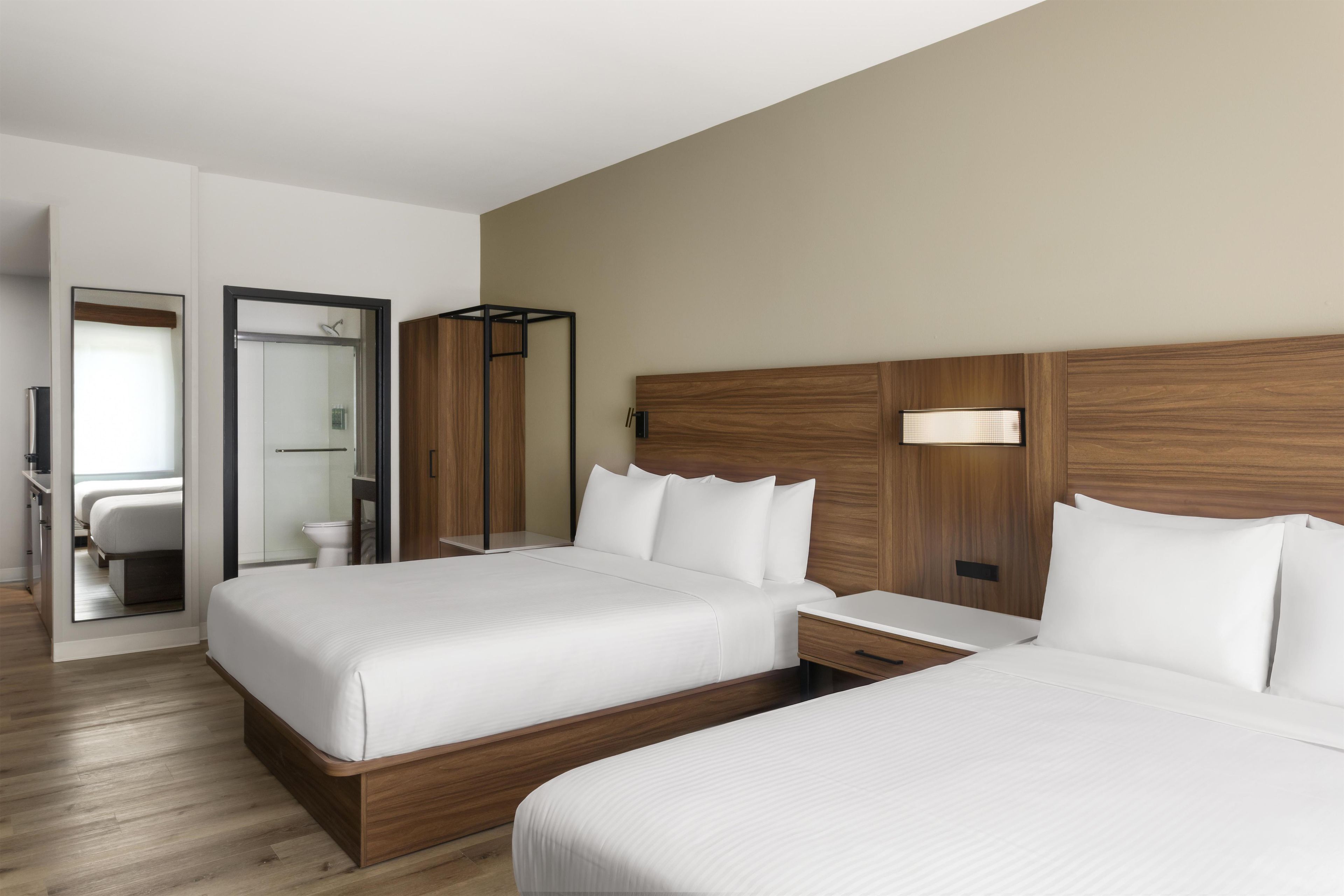 Una habitación de hotel con dos camas, un cabecero de madera, una mesita de noche y un espejo.