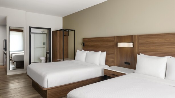 A hotel room with two beds, a wooden headboard, a bedside table, and a mirror.
