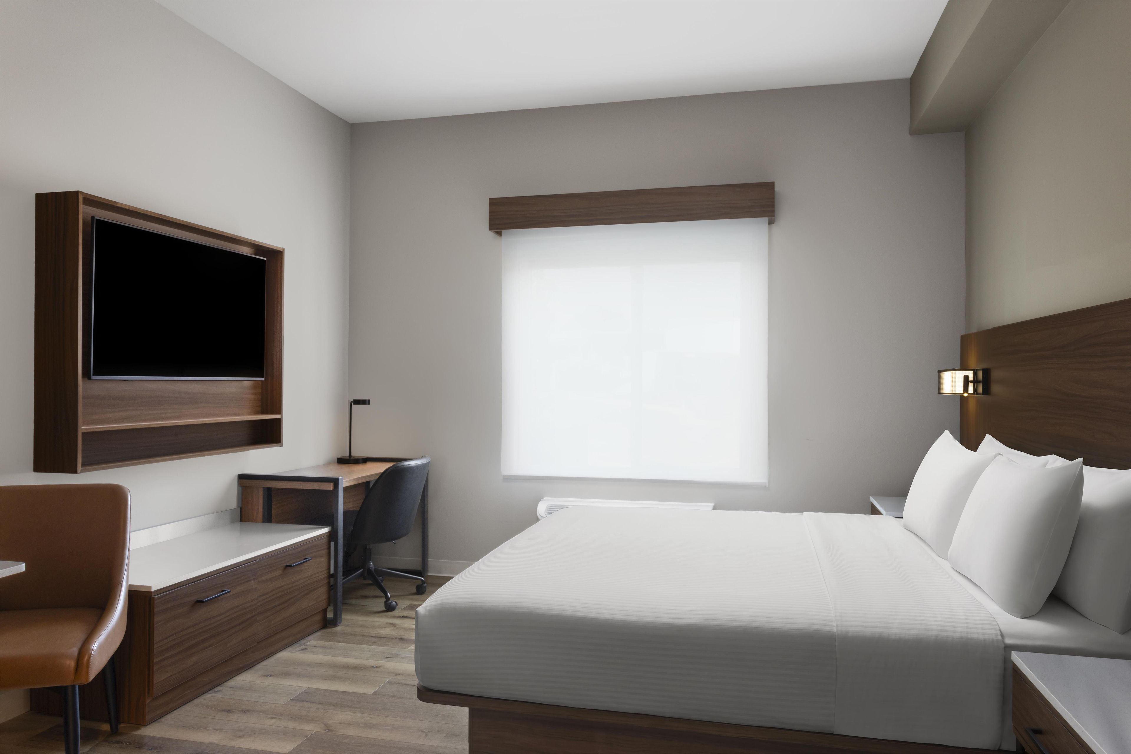 Une chambre d’hôtel moderne avec un grand lit, un bureau, une chaise, une télévision et une fenêtre.