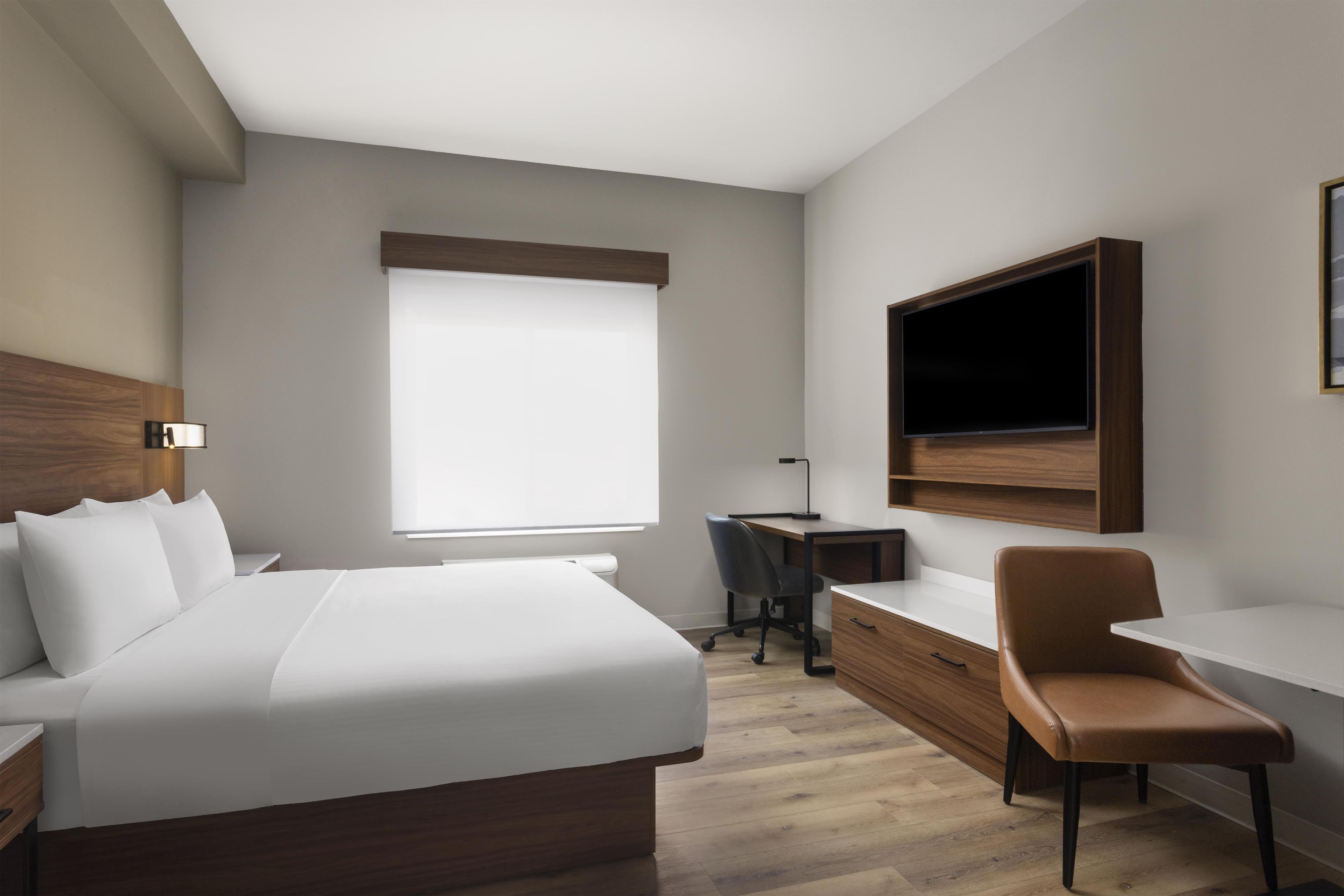 A hotel room with a bed, desk, chair, and a TV mounted on the wall.