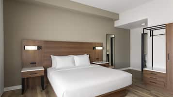 A modern hotel room with a large bed, wooden headboard, bedside tables, a mirror, and a wardrobe.