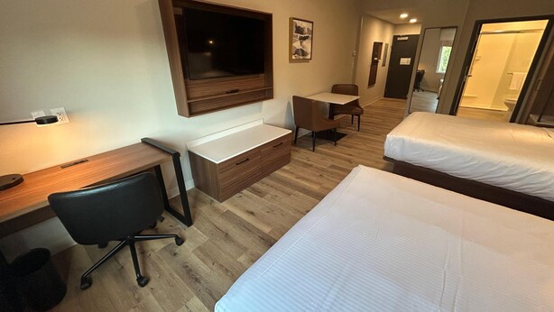 A hotel room with a desk, chair, two beds, a TV, and a small table. - @HOME by Best Western McDonough Atlanta South (McDonough)