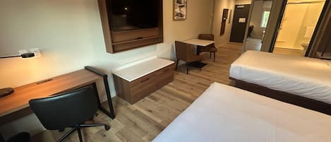 A hotel room with a desk, chair, two beds, a TV, and a small table.