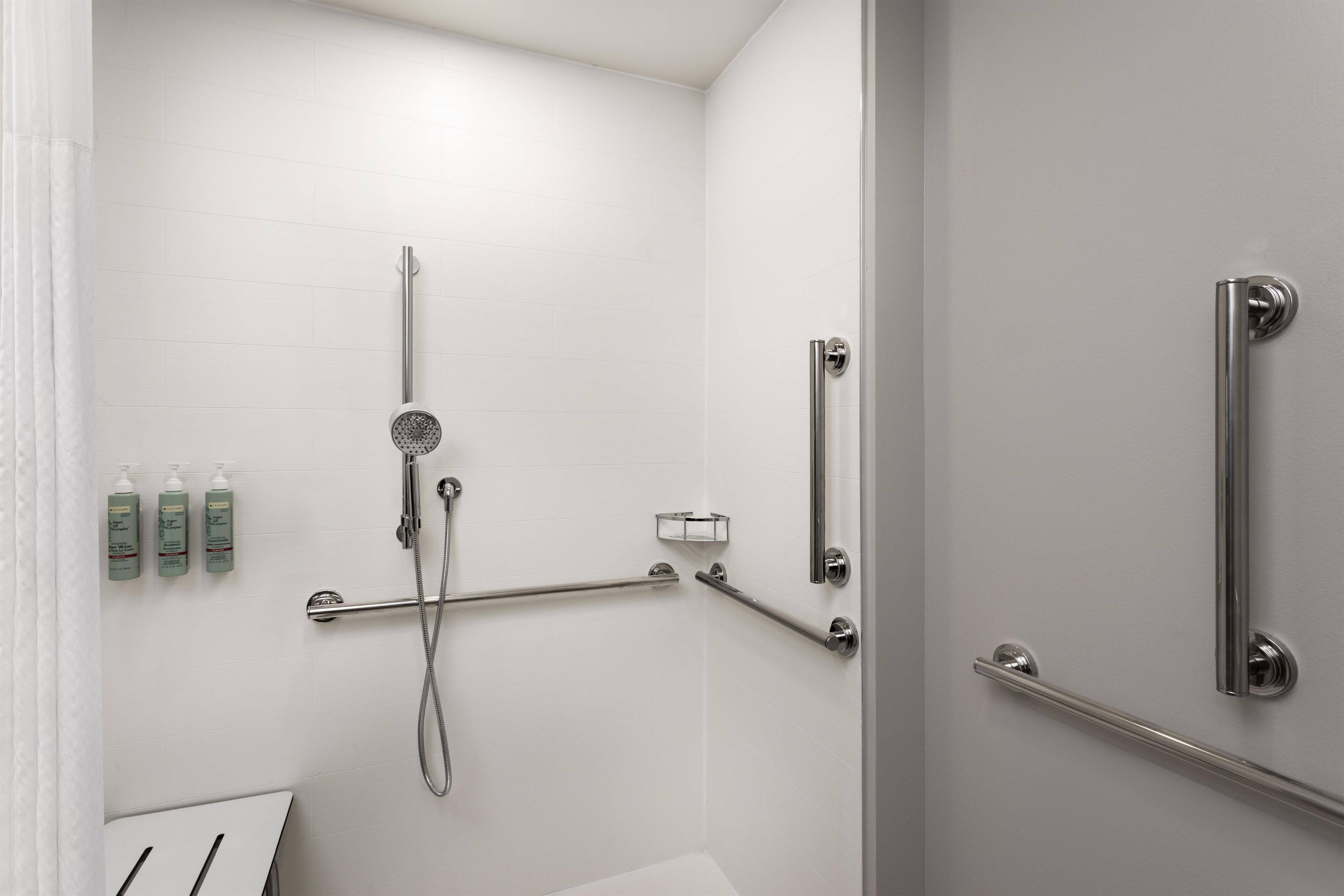 Un baño moderno con ducha, barras de apoyo y artículos de aseo en la pared.