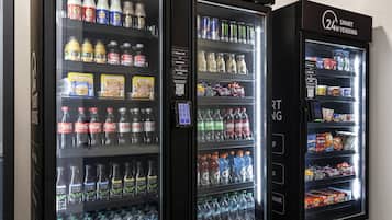 Trois distributeurs automatiques de boissons proposent une variété de produits, notamment des sodas, des jus de fruits et de l’eau en bouteille.