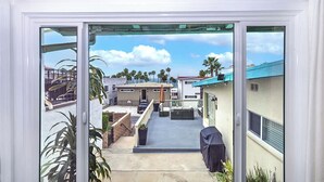 Blick durch eine Schiebetür auf eine Wohngegend mit Terrasse, Gartenmöbeln und einem überdachten Grillplatz.