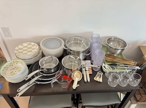 A table with kitchenware including plates, bowls, pots, measuring cups, and utensils.