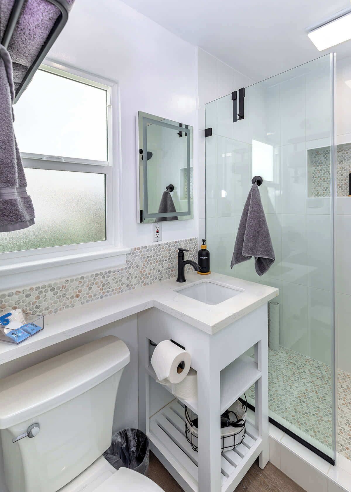 A bathroom with a toilet, sink, mirror, and glass shower enclosure.