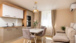 A modern kitchen with white cabinets, a dining table with chairs, a sofa, and a window with curtains. - Luxury Flat in Split City Center 15 min walk from Ferry Port and Beach (Split)