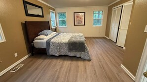 Ein Schlafzimmer mit einem Bett, zwei Fenstern, einer Tür und einer Deckenleuchte.