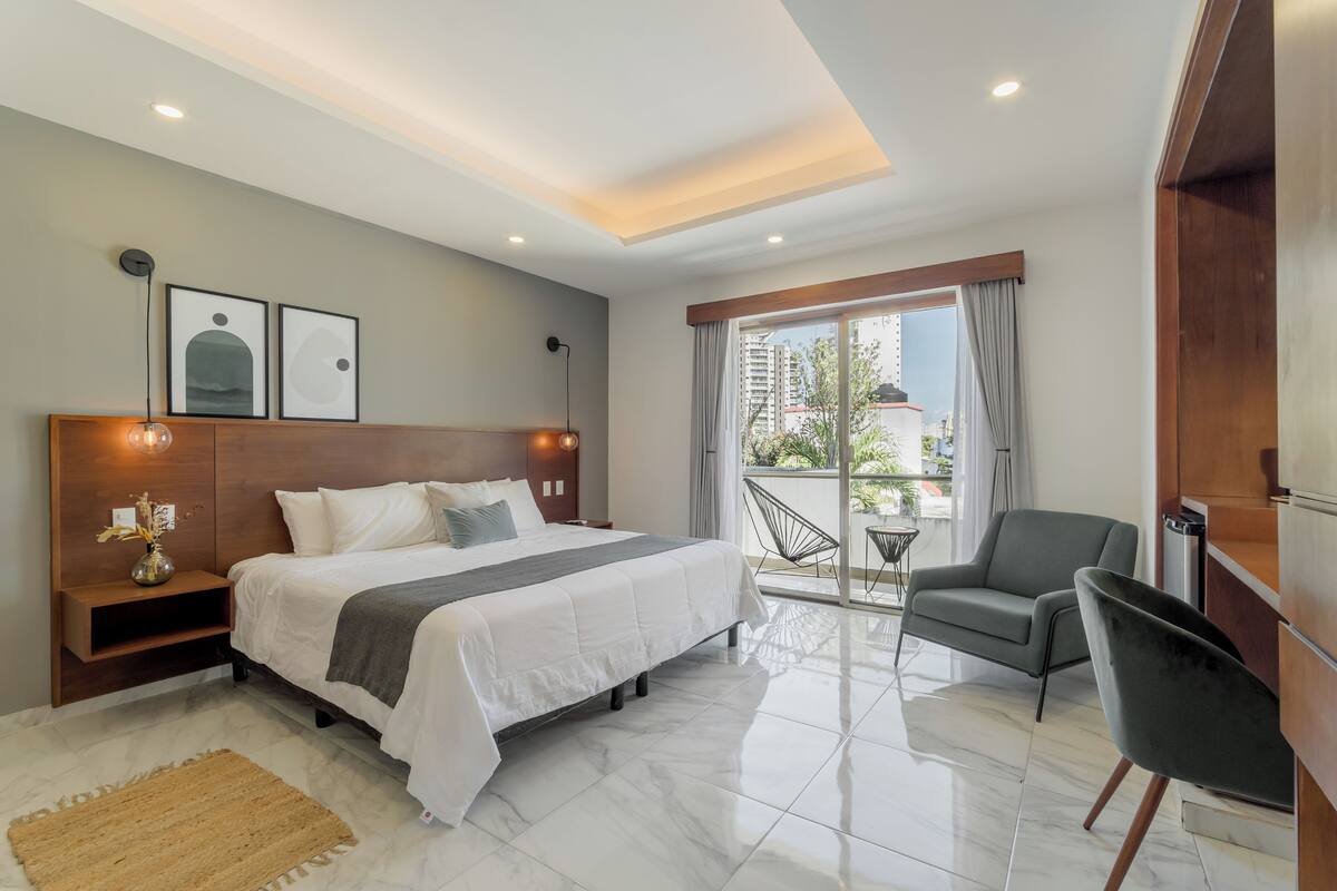 A modern hotel room with a large bed, a balcony with a chair, and a view of the city.