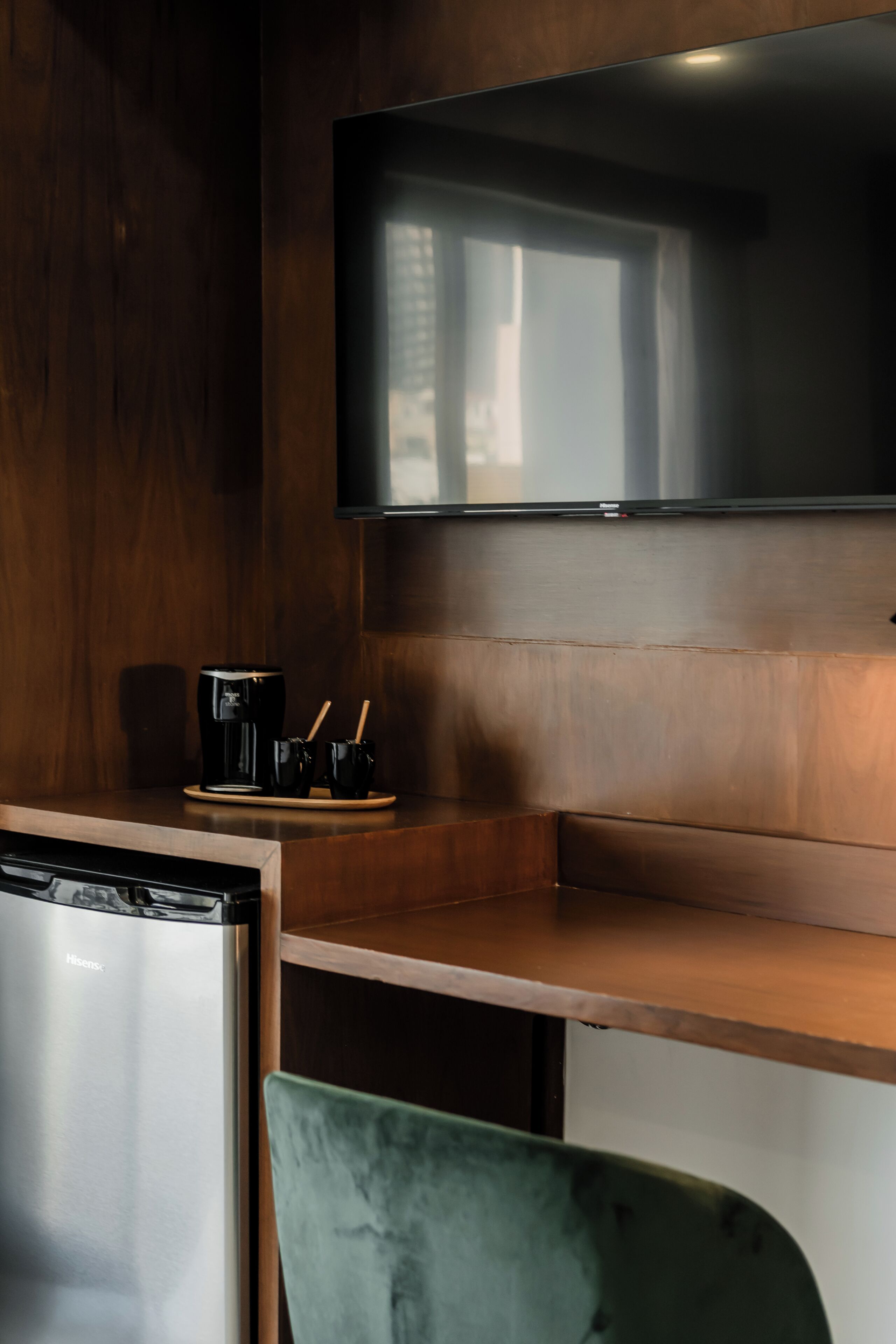 Eine Küchenzeile mit Kaffeemaschine, einem grünen Sessel und einem flachbildfernseher, der an einer Holzwand befestigt ist.