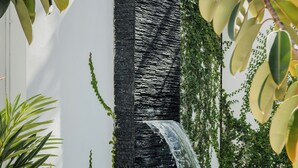 A pool area with a waterfall feature, lounge chairs, and greenery.