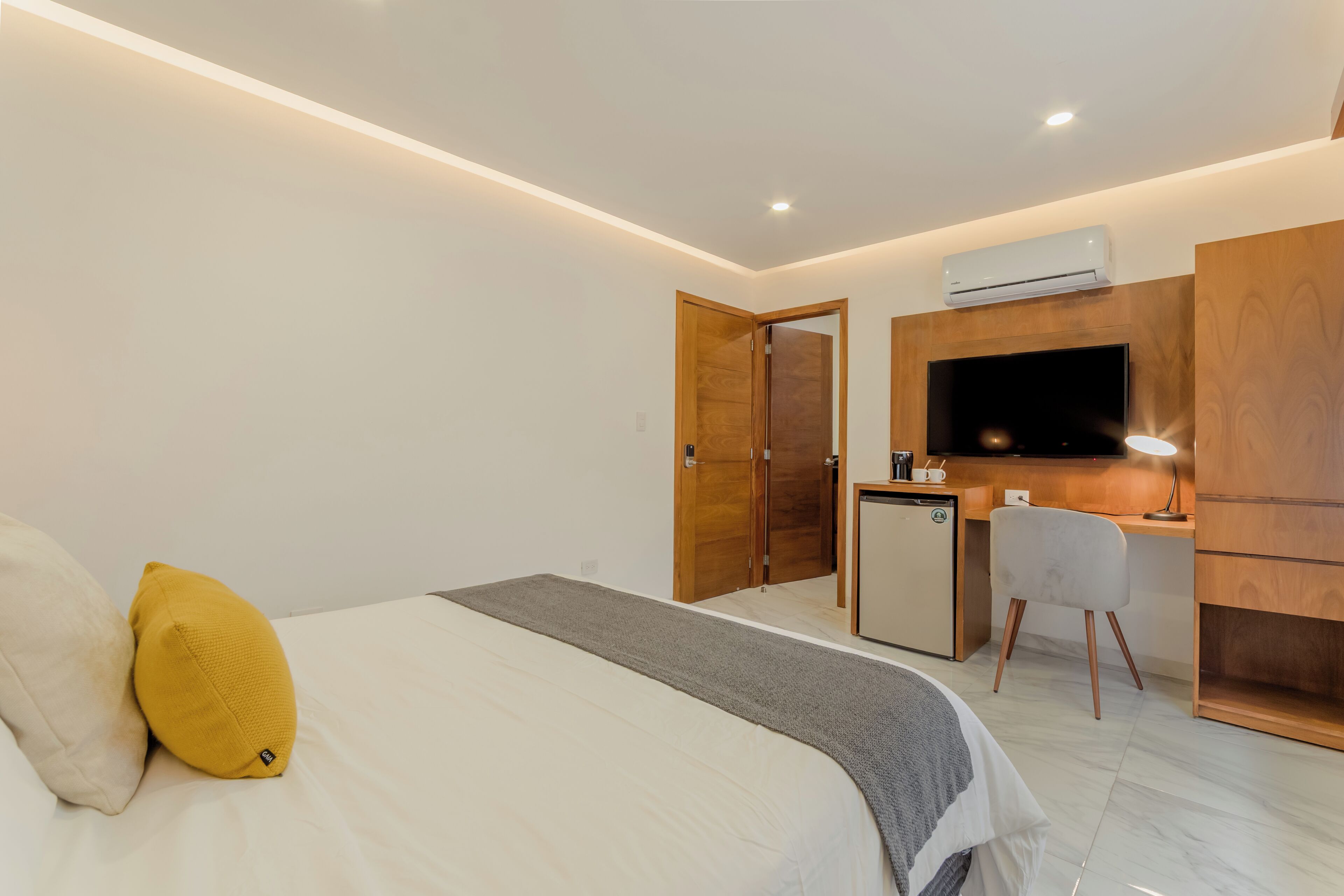 A hotel room with a bed, a desk, a chair, an air conditioner, and a television.