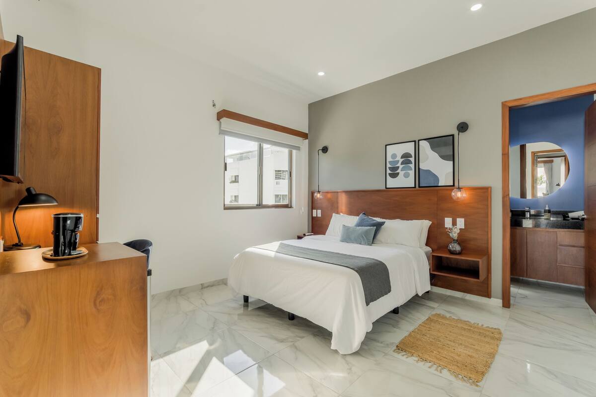 A modern bedroom with a bed, bedside table, lamp, and a view of the outside.