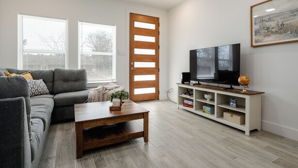 A living room with a sofa, coffee table, TV, and entertainment unit. - Brand New Home Near Downtown (Sulphur Springs)
