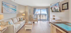 Ein Wohnzimmer mit Sofa, Sessel, Couchtisch und Meerblick vom Balkon aus.