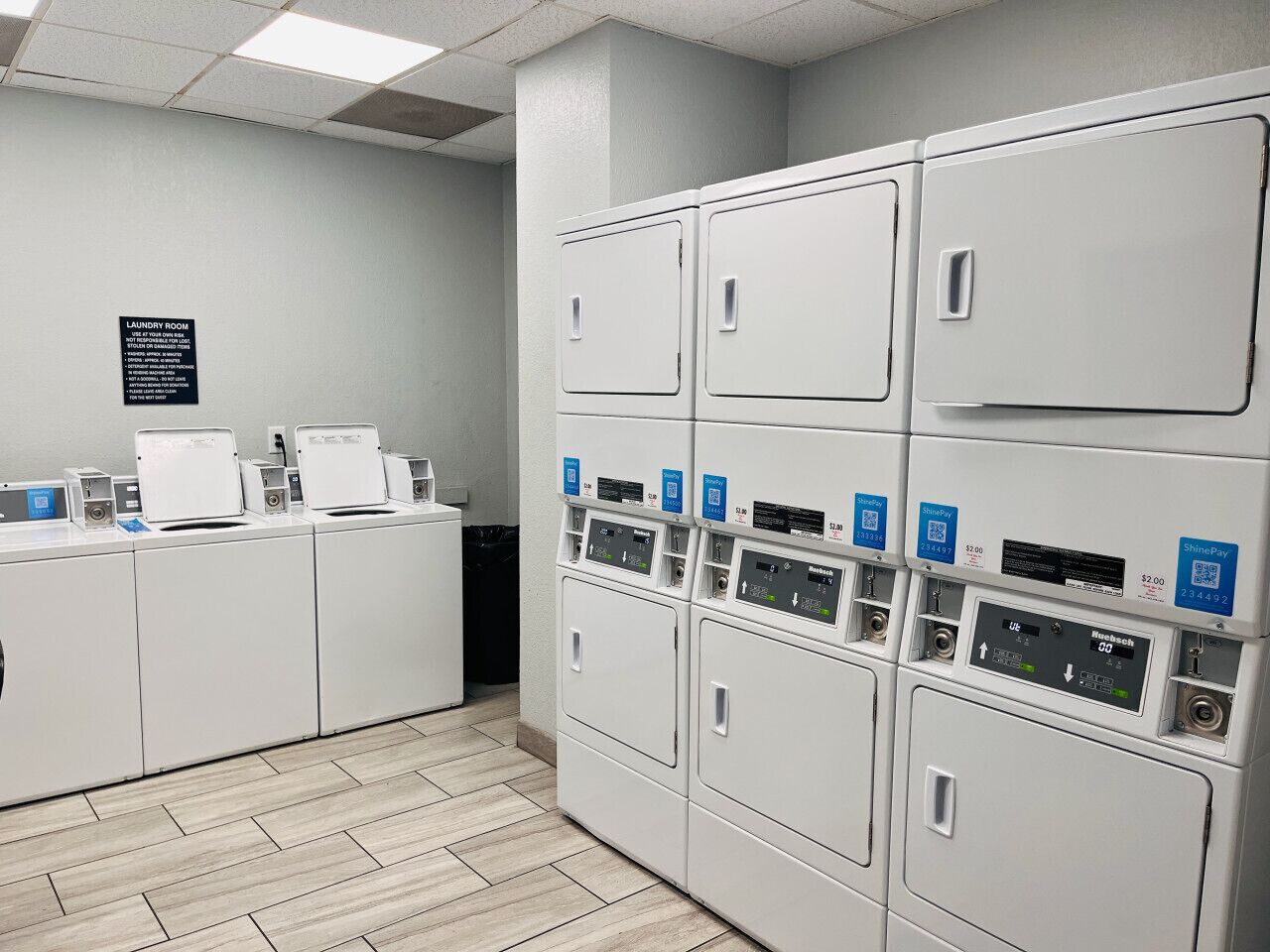 A laundry room with multiple washing machines and dryers, a sign indicating the room's purpose, and a payment terminal.