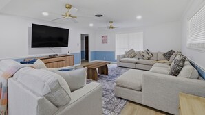 Una sala de estar con una televisión de pantalla plana, dos sofás, una mesa de centro y ventiladores de techo.