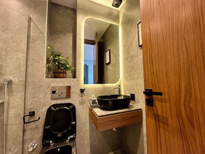 A modern bathroom with a large mirror, a black sink, a wooden vanity, a shower, and a potted plant.