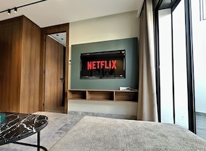 Un soggiorno moderno con una grande TV a schermo piatto montata su una parete verde, scaffali in legno sottostanti e una grande finestra sulla destra.
