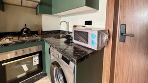 A compact kitchen with a stove, sink, and washing machine, and a door with a handle.