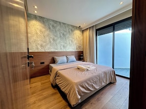 Una camera da letto moderna con un letto grande, una testiera, un comodino, una lampada a parete e vista sull'esterno.