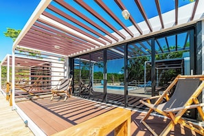 A modern outdoor deck with wooden furniture, a glass-enclosed pool, and a clear view of the surrounding landscape.