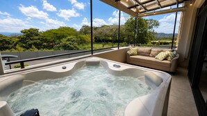 A hot tub with a view of greenery and hills, a beige sofa with patterned cushions, and a pergola with string lights. - Luxury 2-Story Penthouse with Private Jacuzzi (Río Oro)