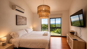 A bedroom with a bed, bedside lamps, a TV, a large window with a view, and a hanging light fixture. - Luxury 2-Story Penthouse with Private Jacuzzi (Río Oro)