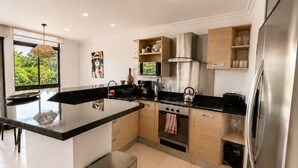 A modern kitchen with a central island, stainless steel appliances, and a view of greenery outside. - Luxury 2-Story Penthouse with Private Jacuzzi (Río Oro)