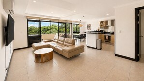 A modern living room with a sofa, a coffee table, and a TV. There is a kitchen area with a dining table and chairs. - Luxury 2-Story Penthouse with Private Jacuzzi (Río Oro)
