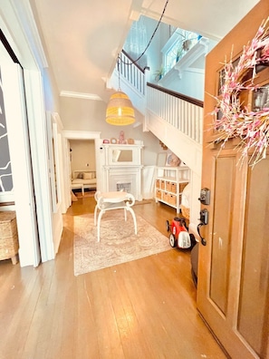 A spacious hallway with a staircase leading to a balcony, a white bench, a toy car, and a decorative wreath on the door. - The Modern Victorian Charmer Hot Tub 5 bedroom 4 bath (Atlanta)